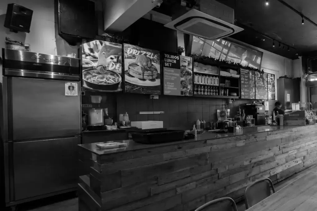 Interior counter of Tolido's Espresso Nook in Singapore with rustic wooden bar, open kitchen, and illustrated brunch menu boards.