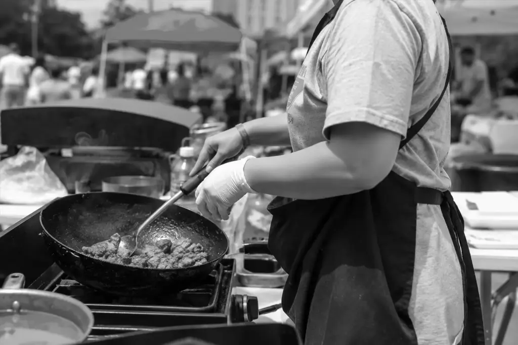 Food vendor stir-frying meat at an outdoor food festival cooking station.