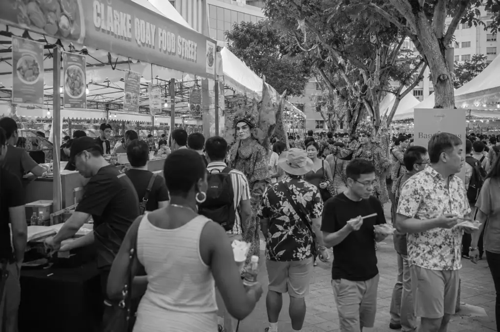 Crowds exploring food stalls and cultural performances at a lively outdoor food festival.