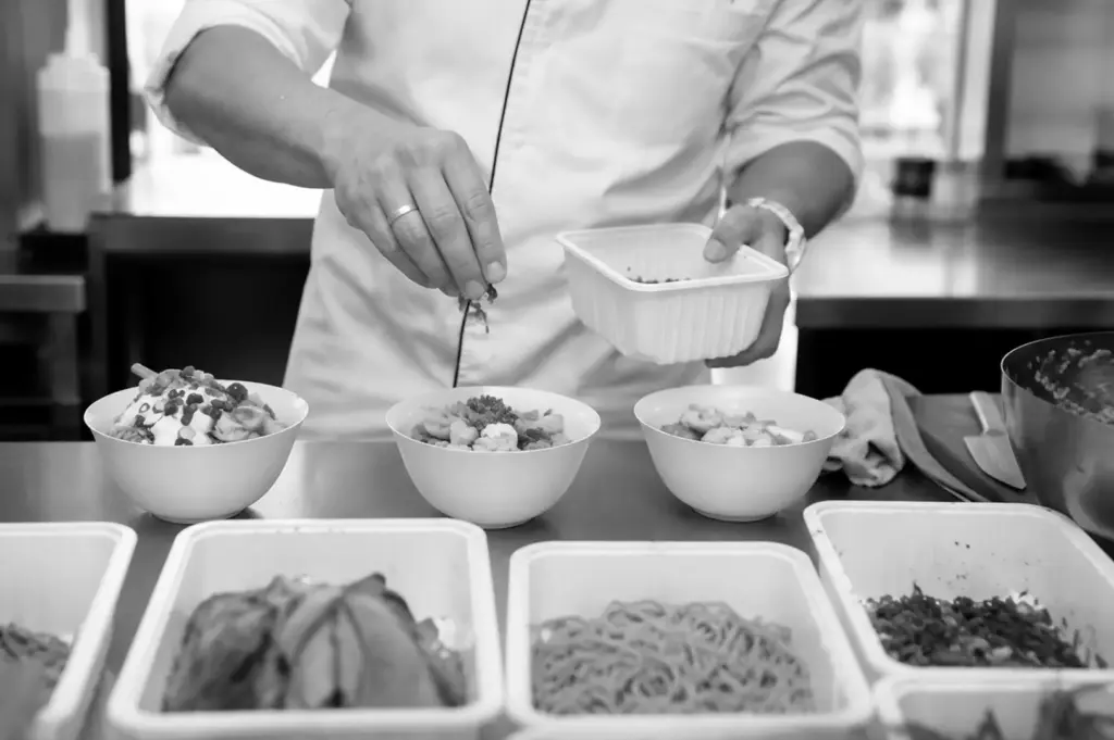 A chef carefully prepares fresh bowls at a pop-up restaurant, showcasing made-to-order meals and the appeal of unique culinary experiences.