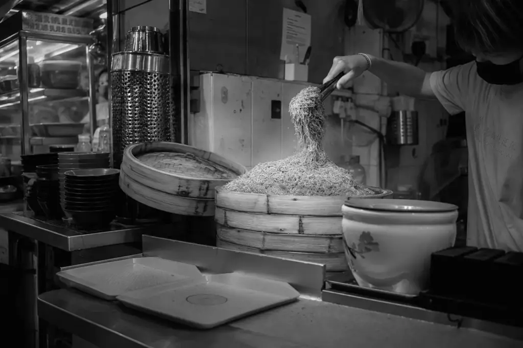 Hawker preparing fresh noodles at a food stall, showcasing the craftsmanship and effort behind quality hawker dishes.