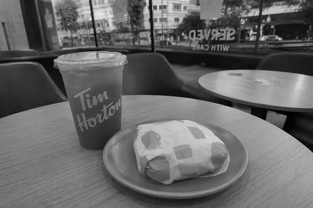 Iced drink and wrapped sandwich on a café table beside large windows overlooking a city street.