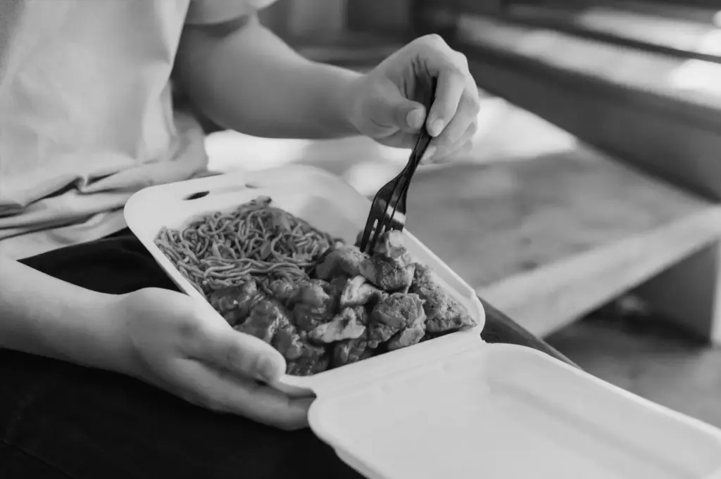 Customer eating a takeaway hawker meal with noodles and roasted meats, reflecting the value and quality consumers expect from local food.