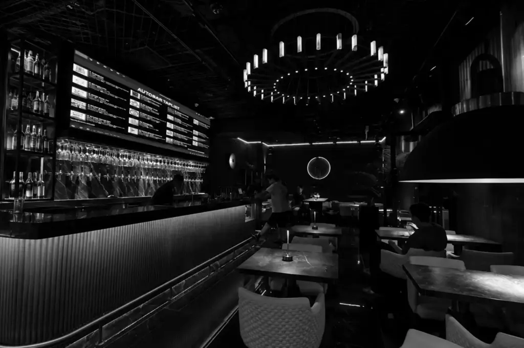 Modern bar interior with illuminated tap wall, tables, and stylish chandelier.