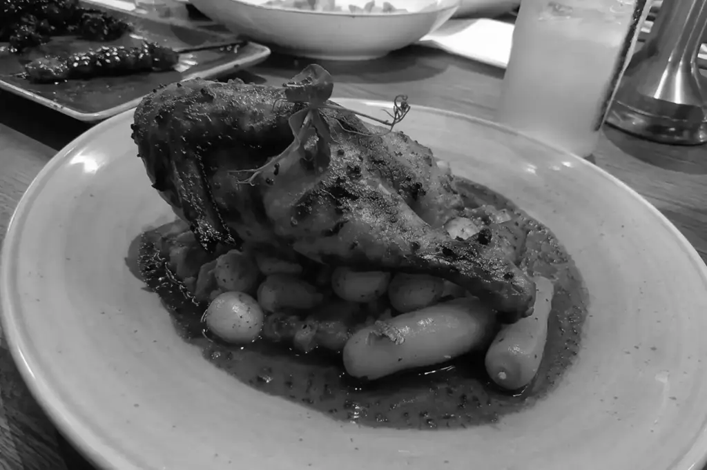 Rotisserie chicken leg served with roasted vegetables and rich savory sauce.