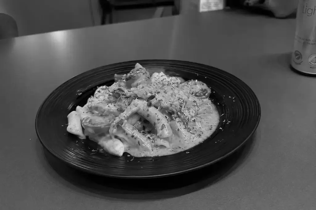 Creamy pasta topped with herbs and grated cheese on a black plate.
