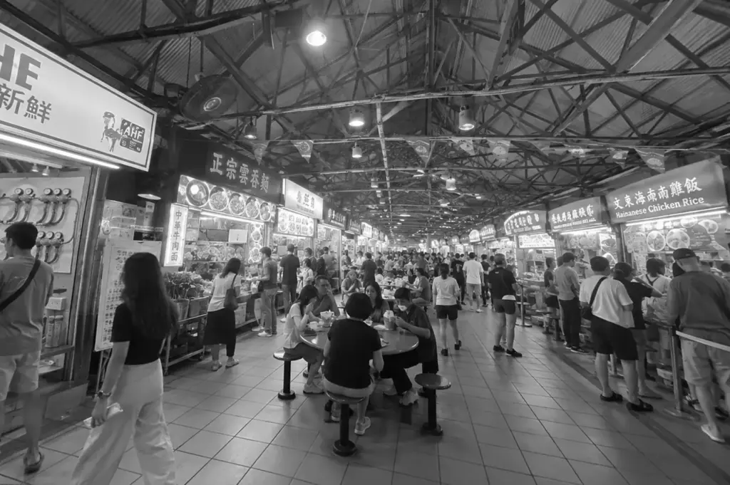 A busy Singapore hawker centre filled with diners, food stalls, and shared tables, highlighting the communal nature of public dining spaces.