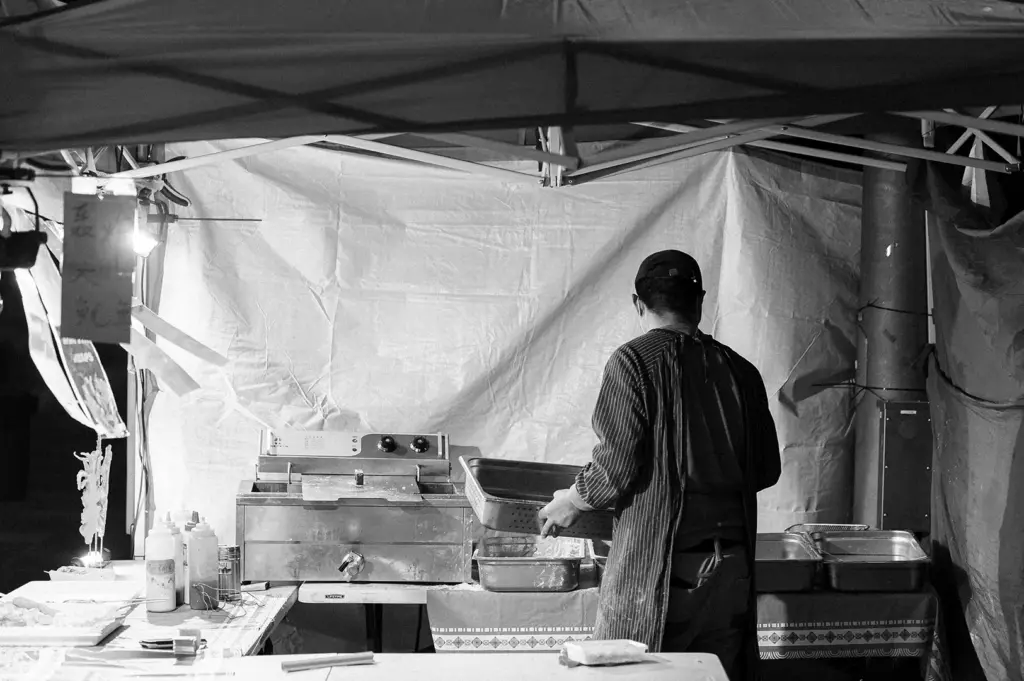A street food vendor prepares food inside a small temporary pop-up stall.