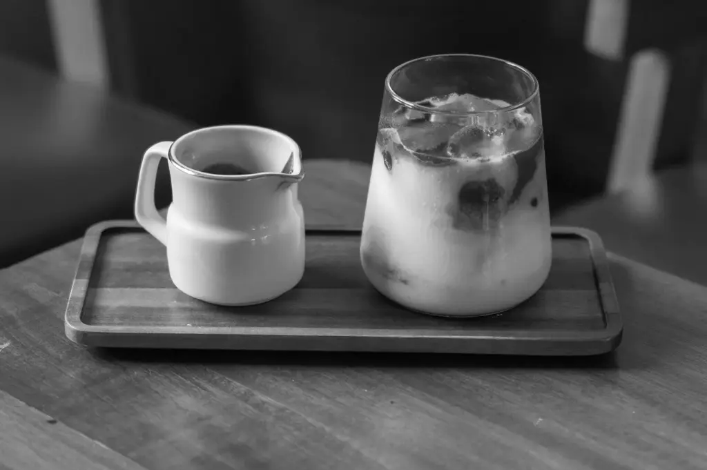 Iced layered matcha drink served with a small pitcher of espresso on a wooden tray.