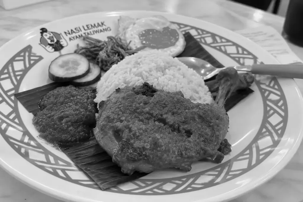 A plate of nasi lemak with coconut rice, fried chicken, sambal, cucumber, anchovies, peanuts, and a fried egg.