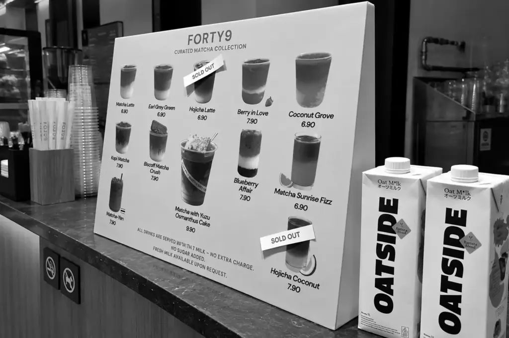 Matcha drink menu display at a café counter with oat milk cartons beside it.