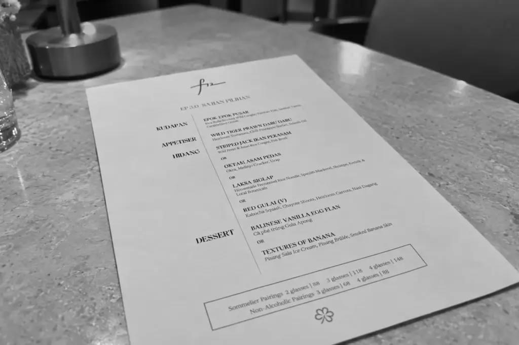 A restaurant menu rests on a table, listing Indonesian-inspired dishes, appetizers, mains, desserts, and beverage pairings.