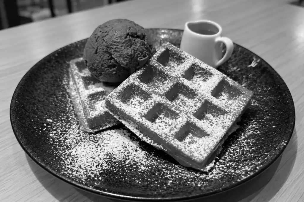 Fresh waffles with a scoop of ice cream and a small pitcher of syrup on a plate.