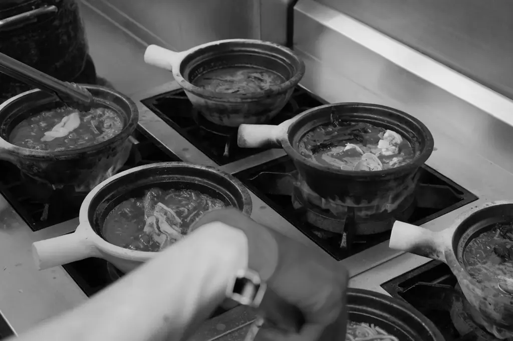 Claypots of seafood soup simmering over multiple burners in a kitchen