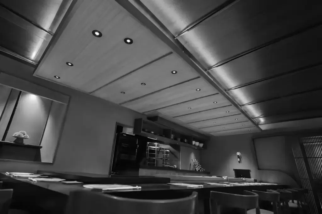 Elegant Japanese sushi restaurant interior with a long counter, warm recessed lighting, and minimalist wood-and-metal decor.