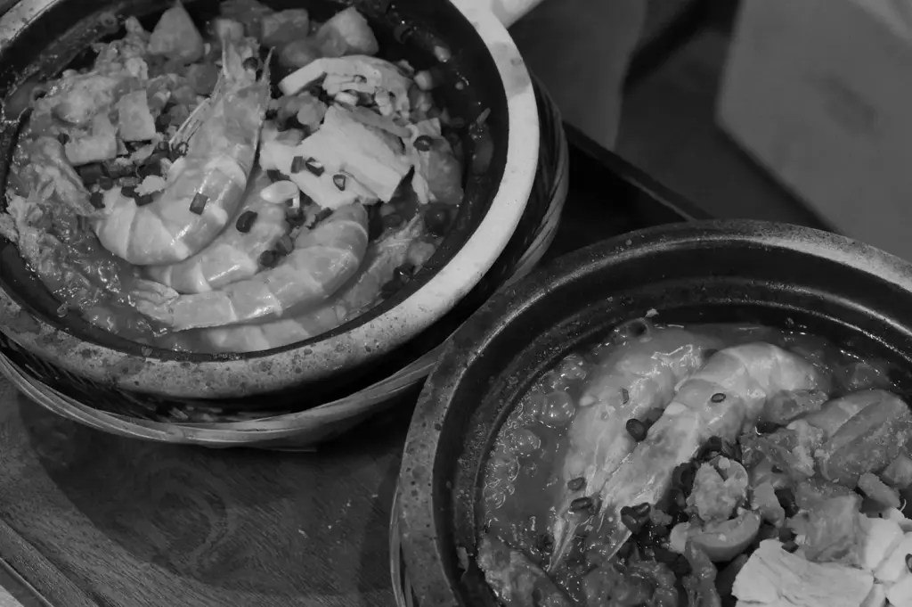 Two claypots filled with prawns, seafood, and rice on a wooden table