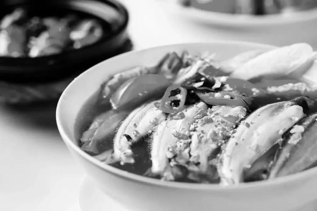 A close-up bowl of fish soup with several pieces of fish and fresh garnishes, photographed from a slightly angled view.