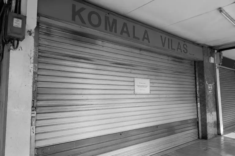 Komala Vilas restaurant in Singapore with its metal roller shutter closed beneath the restaurant signboard.