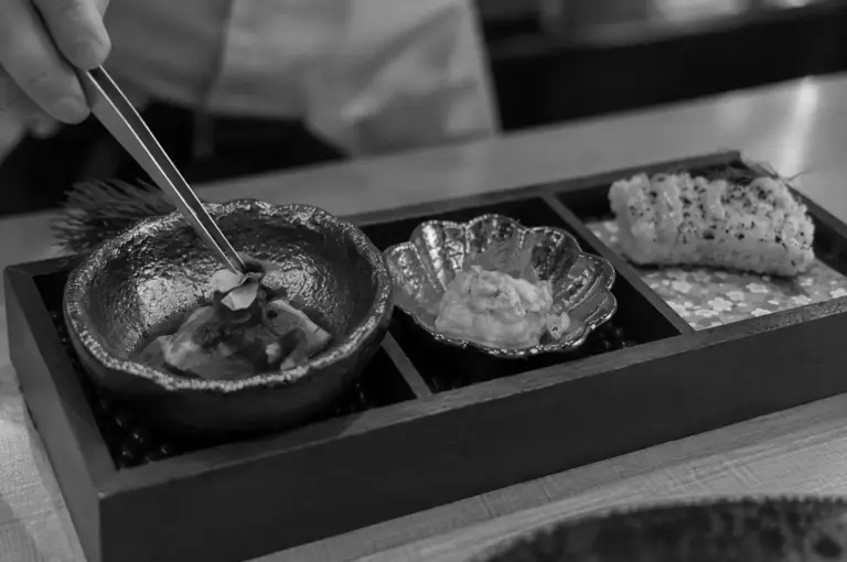 A chef carefully plating a fine-dining dish with tweezers, highlighting precision and attention to detail.