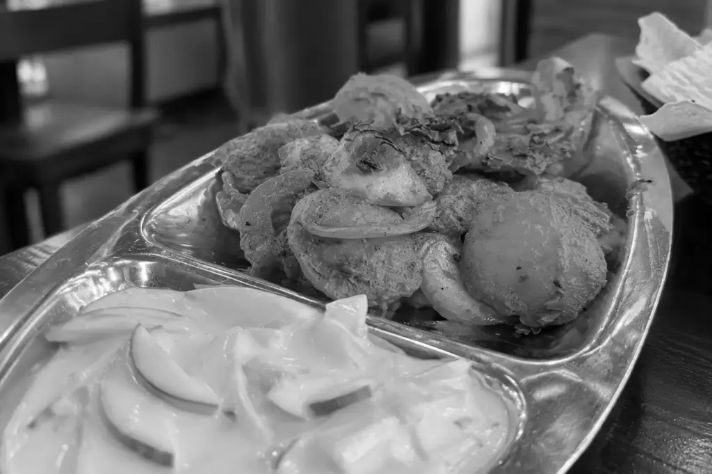 An Indian food platter with assorted savoury snacks, curry and dipping sauces served on a stainless steel tray.