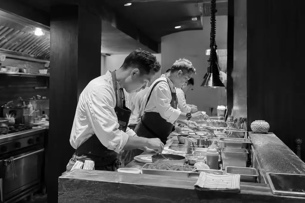 Chefs preparing dishes at a restaurant kitchen counter, highlighting culinary craftsmanship and attention to detail.