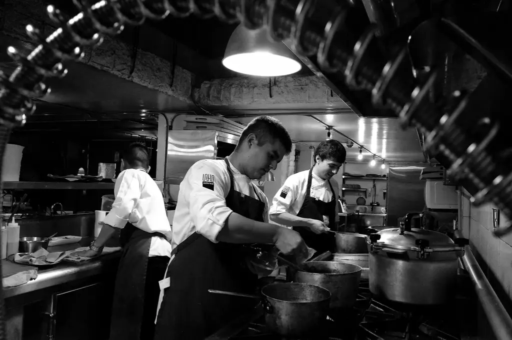Chefs working together in a busy professional kitchen, preparing dishes under focused lighting.