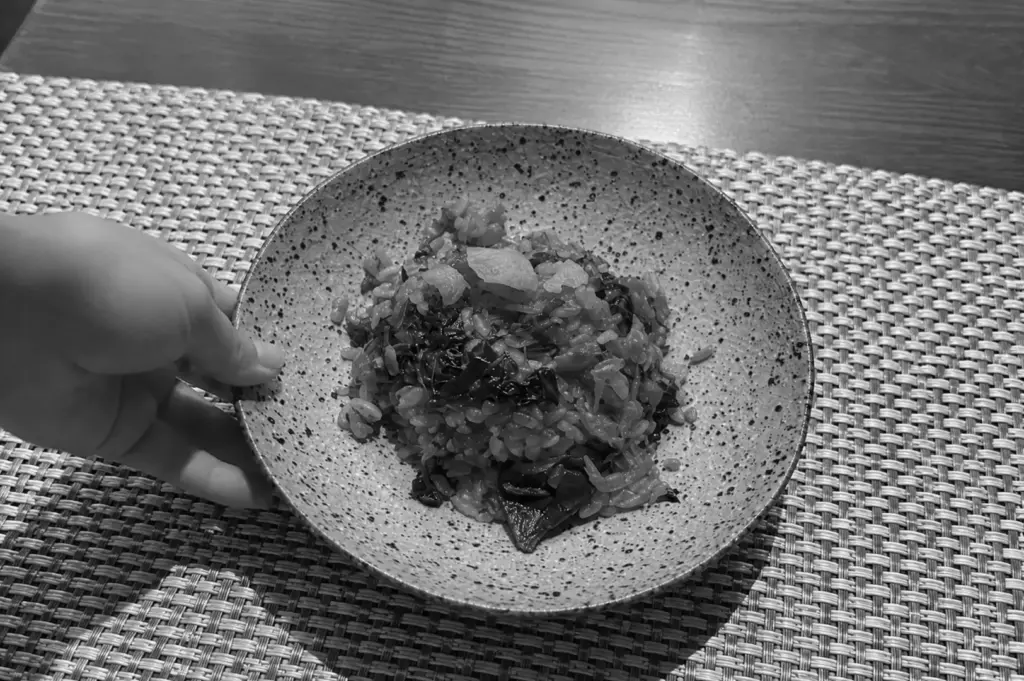 A hand presenting a bowl of rice in a speckled ceramic dish on a woven placemat at a restaurant.