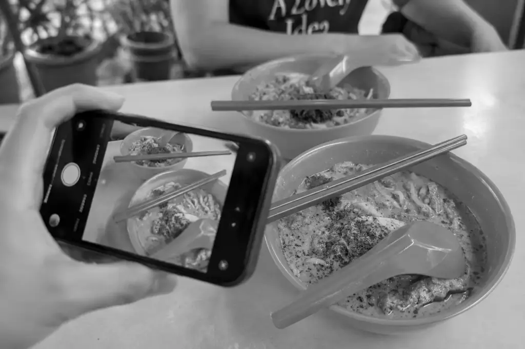 A diner using a smartphone to photograph traditional noodles, capturing the connection between heritage food and modern social media storytelling.