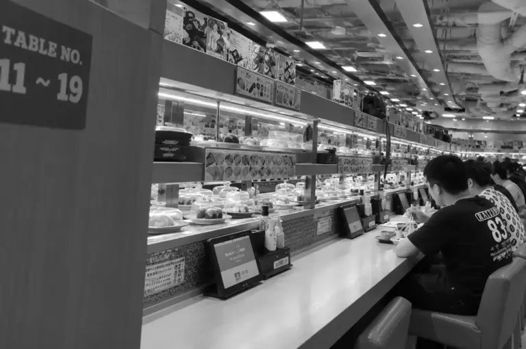 Sushi conveyor belt restaurant interior with diners seated at the counter.